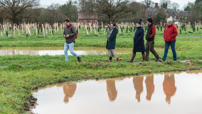 A group of people walking around a pond in the Commemorative Woodland at Erddig.